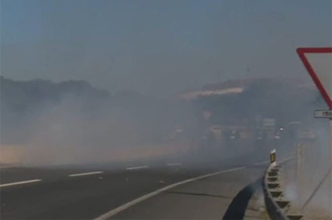 Imagen de la carretera de acceso al Valle de Escombrera con humo por la quema de neum&aacute;ticos y el lanzamiento de botes de humo